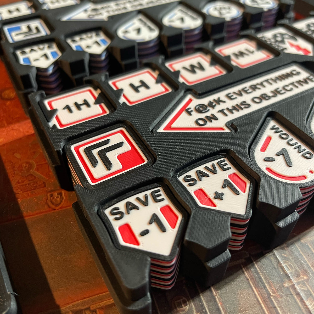 ttr-327-detail-red: Red accent tokens stacked in the case, Save and Wound modifiers in close up